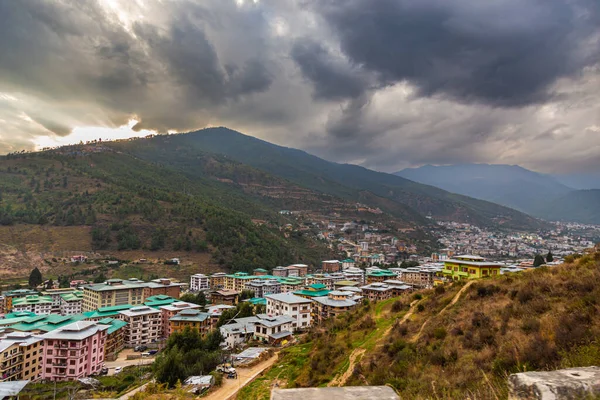 Thimphu, Butan - 26 Ekim 2021 Bhutan başkentinin havadan görünüşlü şehir manzarası. Şehrin üzerinde dramatik bulutlu gökyüzü manzaralı. Butan 'ın dağ vadisindeki en büyük şehri. Yeşil çatılı evler