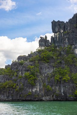 Malezya, Langkawi sahilinin dağ silueti. Tropikal bitki örtüsüyle kaplanmış kayalar. Bulutlar güneşin ve mavi gökyüzünün önüne doğru ilerliyor. Langkawi Adası turizm merkezi. Manzara manzarası