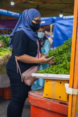 Kuala Lumpur, Malezya - 21 Haziran 2022: Türban veya başörtüsü takmış Müslüman bir kadın, sokak pazarındaki bir sebze standında doğru sebzeleri arıyor. Malezya 'da taze pazarlar çok popülerdir.