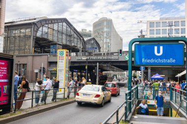 Berlin, Germany - June 29, 2022: Berlin Friedrichstrasse train station with the stairs to the subway or metro station. Busy place in East Berlin. People are waiting for the tram. A Taxi car passing