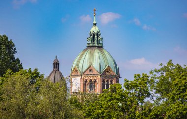 Münih, Almanya - 6 Temmuz 2022: St. Luke Kilisesi (St. Lukas veya Lukaskirche). Isar kıyılarında, Steinsdorfstrae ve Mariannenplatz arasında yer alır. Ağaçların arasından bak