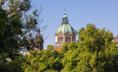 Munich, Germany - July 6, 2022: St. Luke Church (St. Lukas or Lukaskirche). Located on the banks of the Isar, between the Steinsdorfstrae and Mariannenplatz.  View through the trees