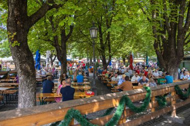 Munich, Germany - July 6, 2022: Beer garden on the viktualienmarkt at lunch time. Locals and tourist relaxing on a summer day under the shady trees and enjoying the Bavarian beer, so called Brotzeit