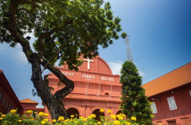 Malacca, Malaysia - August 10, 2022: Christ Church in the center of Melaka. Oldest functioning Protestant church in Malaysia. Past the trees and flowers of the park on the Dutch square or red square.