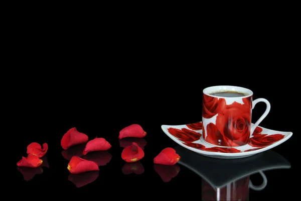 Taza de café rojo entre pétalos de rosa sobre el fondo negro — Foto de Stock