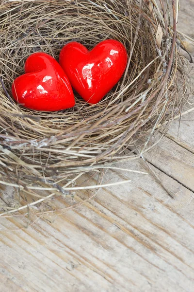 Deux cœurs rouges dans un nid d'oiseaux sur une planche de bois — Photo