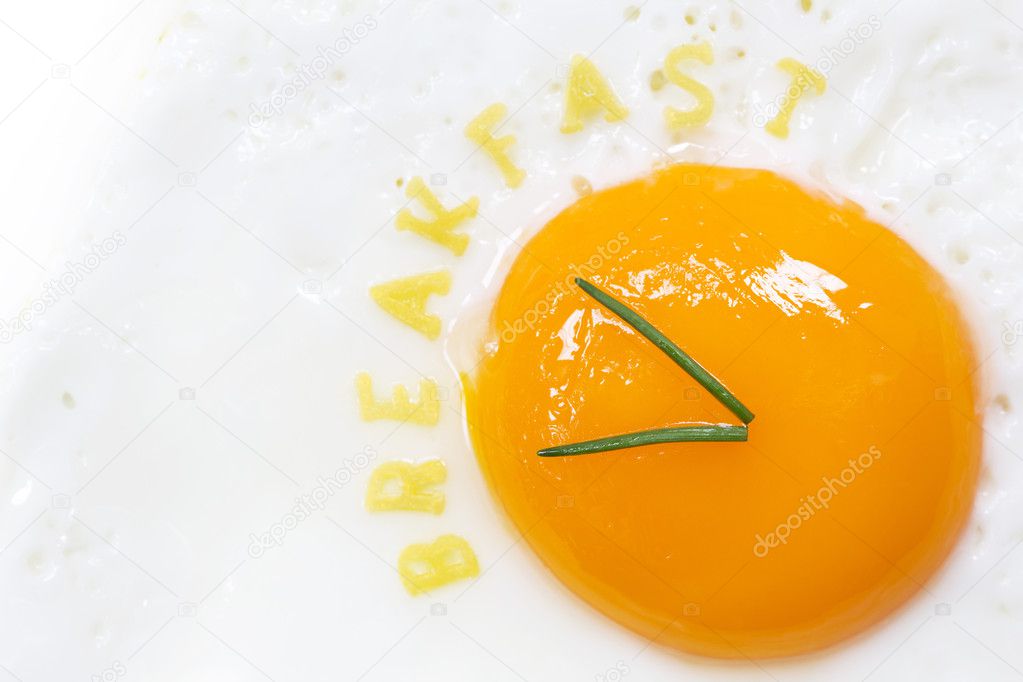 Fried egg sunny side up in form of a clock with noodle letters for breakfast
