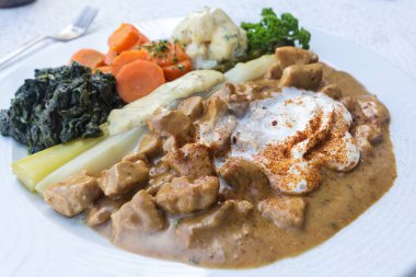 Zürih usulü dana eti güveci ve çeşitli mevsimlik sebzeler: asparageller, havuçlar, kalifer, döner ve krema sosu. Beyaz tabakta yerel İsviçre mutfağı.