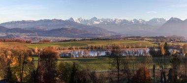 Gerzensee Gölü 'nün panorama görüntüsü ve Alpler' in karlı dağları ve akşam sisi olan köyler öğleden sonra parlıyor. 