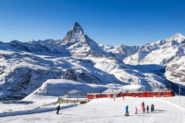 Zermatt, Switzerland - January 06. 2022: Matterhorn - the most famous landmark in Swiss Alps mountains with popular skiing area and the red tourist train.