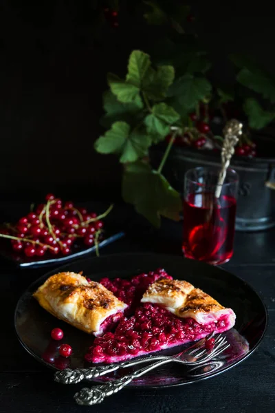 Red currant pie from recipe of Berry Galette with cut slice and vintage forks and a glass of red currant juice - dark and moody