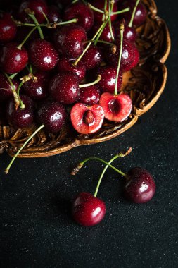 Taze kırmızı kirazlar, ahşap bir tabakta, üzerinde su damlacıkları olan, koyu ve karamsar.