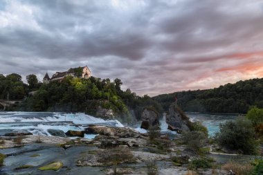 Rhine Falls - the largest waterfall in Europe, with Castle Laufen on the hill in sunset hour with dramatic and stormy clouds