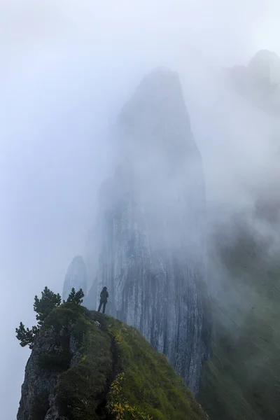 A hiker standing in front of the famous Swiss Alps peak Saxer Lucke with stunning rock formation in rising mist and fog