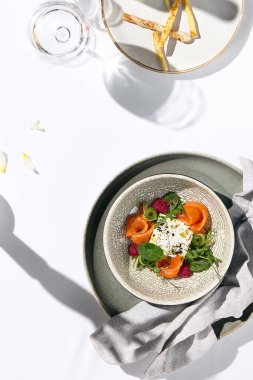 Somon, salatalık ve pancar ile ev yapımı peynir salatası. Beyaz masada somon salatasıyla akşam yemeği ve basit çağdaş dekorasyon. Güneş ışığı ve sert gölge, hayat devam ediyor. Somon salatası kasesi