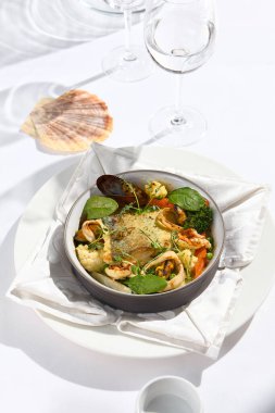 Balık ve sebzeli güzel deniz ürünleri güveci. Sağlıklı balık tabağı - fırında balık, karides, brokoli ve domates üzerine midye. Yaz günü gölgeli beyaz masa örtüsü ve cam servis ediyorum.