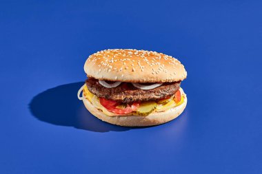 Sert gölgeli sığır burger mavisi arka plan. Amerikan abur cuburu çok az. Hamburger modasına uygun. Basit burger rengi arkaplan