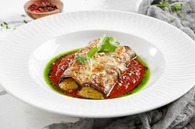 Domates ve peynirle doldurulmuş patlıcan ruloları. Fırında patlıcan ve peynirli rollatini. Patlıcan aperatifi taştan arka planda beyaz tabakta. Bitki tabanlı menü