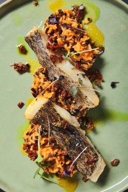 Siyah arka planda yeşil tabakta dilimlenmiş beyaz balıklı risotto. Kahverengi ve yabani pirinç karışımlı ızgara morina balığı. Asgari bileşim: Tekstil ile siyah masada balık ve risotto