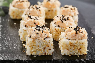 Karanlık taş masada Maki suşisi. Deniz kabuğu ve yengeçli suşi rulosu. Siyah arkaplan, yapraklar ve sert gölgeli japon tarzı menü