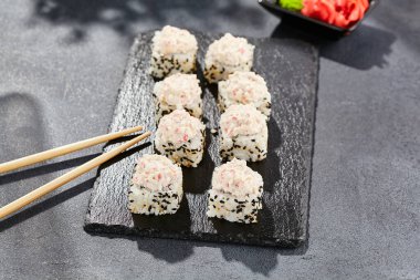 Karanlık taş masada Maki suşisi. Deniz kabuğu ve yengeçli suşi rulosu. Siyah arkaplan, yapraklar ve sert gölgeli japon tarzı menü