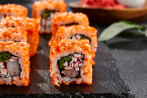 Maki sushi on dark stone table. California maki with tobiko. Sushi roll with crab,shrimp, cucumber inside, maguro outside. Style concept japanese menu with black background, leaves and hard shadow