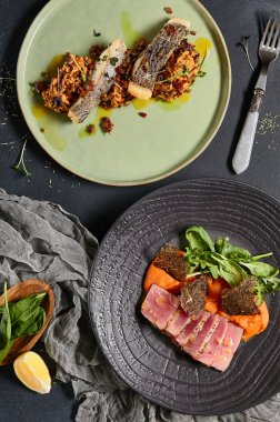 Tabaktaki balıktan. Dilimlenmiş beyaz balıklı risotto, domates soslu ton balığı bifteği ve nori. Koyu arkaplanda moda bir kompozisyon. Siyah masadaki balıkların en az bileşimi.