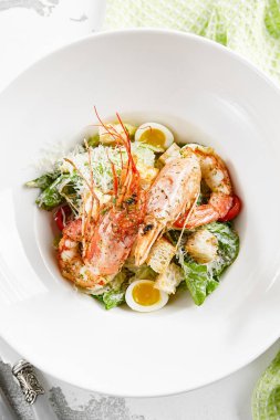 Taş masada beyaz tabakta karidesli klasik Sezar salatası. Restoranda İtalyan menüsü. Köy tarzında deniz mahsulleri sezarı. Izgara karides, yeşil yaprak, yumurta, kızarmış ekmek ve peynirli moda salata.