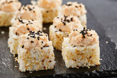 Karanlık taş masada Maki suşisi. Deniz kabuğu ve yengeçli suşi rulosu. Siyah arkaplan, yapraklar ve sert gölgeli japon tarzı menü