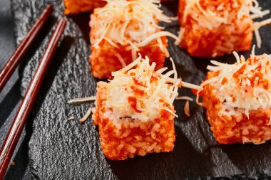 Karanlık taş masada Maki suşisi. Tobiko ile Kaliforniya maki 'si. İçinde balık olan suşi, dışında peynirli maguro. Siyah arka planı, yaprakları ve sert gölgesi olan Japon tarzı bir menü.