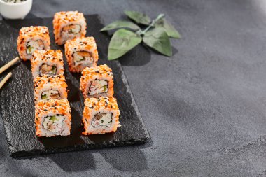 Kara tahtada Maki suşisi. Masaj ve susamlı California maki 'si. Yengeçli suşi, içeride salatalık, dışarıda tobiko. Siyah arka planı, yaprakları ve sert gölgesi olan Japon tarzı bir menü.