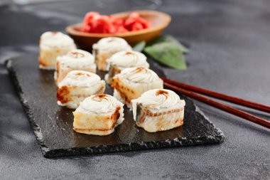 Kara tahtada Maki suşisi. Yılanbalıklı Unagi maki. Yılanbalığı, krem peynir ve unagi soslu suşi. Siyah arka planı, yaprakları ve sert gölgesi olan Japon tarzı bir menü.