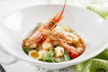 Taş masada beyaz tabakta karidesli klasik Sezar salatası. Restoranda İtalyan menüsü. Köy tarzında deniz mahsulleri sezarı. Izgara karides, yeşil yaprak, yumurta, kızarmış ekmek ve peynirli moda salata.