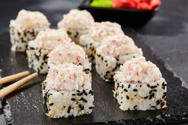 Karanlık taş masada Maki suşisi. Deniz kabuğu ve yengeçli suşi rulosu. Siyah arkaplan, yapraklar ve sert gölgeli japon tarzı menü