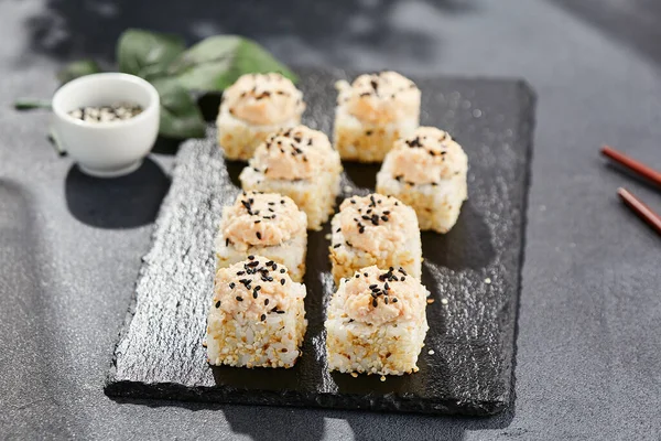 Maki sushi on dark stone table. Sushi roll in seasame and crab topped. Style concept japanesse menu with black background, leaves and hard shadow