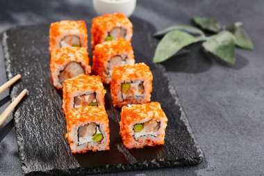 Karanlık taş masada Maki suşisi. Tobiko ile Kaliforniya maki 'si. Peynirli suşi, karides, içinde avokado, dışında maguro. Siyah arka planı, yaprakları ve sert gölgesi olan Japon tarzı bir menü.