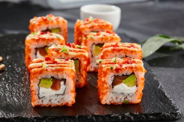 Karanlık taş masada Maki suşisi. Tobiko ile Kaliforniya maki 'si. Peynirli suşi, somon, içinde avokado, dışında maguro. Siyah arka planı, yaprakları ve sert gölgesi olan Japon tarzı bir menü.