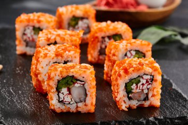 Karanlık taş masada Maki suşisi. Tobiko ile Kaliforniya maki 'si. Yengeçli suşi, karides, içeride salatalık, dışarıda maguro. Siyah arka planı, yaprakları ve sert gölgesi olan Japon tarzı bir menü.