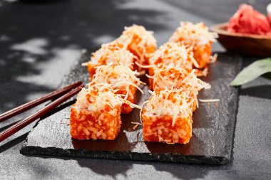 Karanlık taş masada Maki suşisi. Tobiko ile Kaliforniya maki 'si. İçinde balık olan suşi, dışında peynirli maguro. Siyah arka planı, yaprakları ve sert gölgesi olan Japon tarzı bir menü.