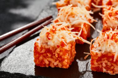 Karanlık taş masada Maki suşisi. Tobiko ile Kaliforniya maki 'si. İçinde balık olan suşi, dışında peynirli maguro. Siyah arka planı, yaprakları ve sert gölgesi olan Japon tarzı bir menü.