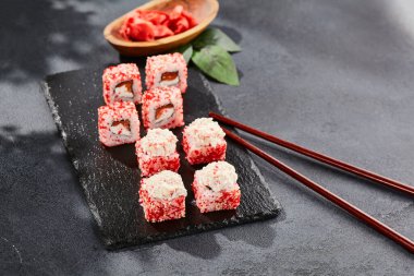 Kara tahtada Maki suşisi. Yengeçli Maki dürümü. Yengeç, krem peynir ve tobika ile suşi rulosu. Siyah arka planı, yaprakları ve sert gölgesi olan Japon tarzı bir menü.