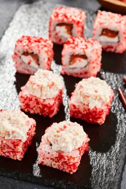 Kara tahtada Maki suşisi. Yengeçli Maki dürümü. Yengeç, krem peynir ve tobika ile suşi rulosu. Siyah arka planı, yaprakları ve sert gölgesi olan Japon tarzı bir menü.