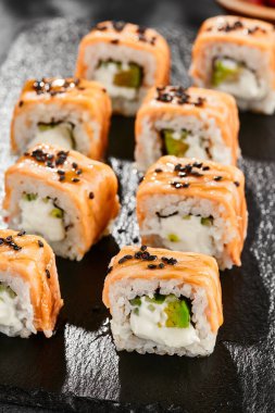 Kara tahtada Maki suşisi. Fırında somonlu sıcak Philadelphia maki. Izgara somon, krem peynir ve avokado ile suşi rulosu. Siyah arka planı, yaprakları ve sert gölgesi olan Japon tarzı bir menü.