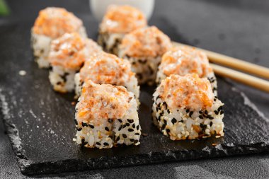 Kara tahtada fırında Maki suşisi. Somon ve peynirli sıcak suşi rulosu. Sushi rulo sushi dışarıda, fırında somon ve peynirli. Siyah arka planı, yaprakları ve sert gölgesi olan Japon tarzı bir menü.