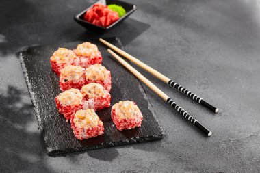 Kara tahtada fırında Maki suşisi. Somonlu sıcak suşi. Dışarıda tobiko ile suşi rulosu, fırında balık ve peynir. Siyah arka planı, yaprakları ve sert gölgesi olan Japon tarzı bir menü.