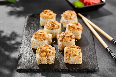 Kara tahtada fırında Maki suşisi. Yılanbalıklı sıcak unagi maki. Fırında yılan balığı, peynir ve unagi soslu suşi rulosu. Siyah arka planı, yaprakları ve sert gölgesi olan Japon tarzı bir menü.