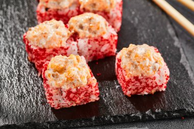 Kara tahtada fırında Maki suşisi. Somonlu sıcak suşi. Dışarıda tobiko ile suşi rulosu, fırında balık ve peynir. Siyah arka planı, yaprakları ve sert gölgesi olan Japon tarzı bir menü.