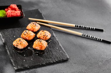 Kara tahtada fırında Maki suşisi. Sıcak unagi maki ve tobiko. Fırında peynirli suşi, masago ve unagi soslu. Siyah arka planı, yaprakları ve sert gölgesi olan Japon tarzı bir menü.