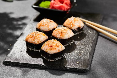 Kara tahtada fırında Maki suşisi. Sıcak unagi maki ve tobiko. Fırında peynirli suşi, masago ve unagi soslu. Siyah arka planı, yaprakları ve sert gölgesi olan Japon tarzı bir menü.