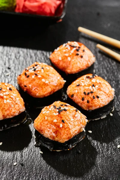 暗いスレート上で焼き巻き寿司 熱々のうなぎ巻きととび子 焼きチーズ マサゴ うなぎソースをトッピングした寿司ロール 黒を基調としたスタイルのコンセプト日本料理 葉とハードシャドウ — ストック写真